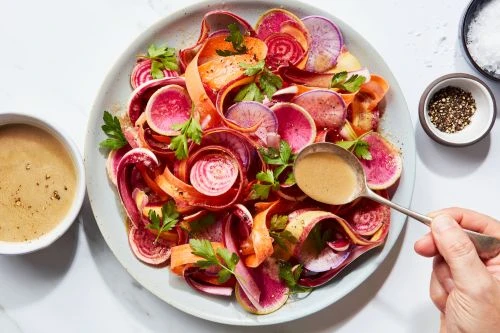 Overhead shot of a colourful salad with sliced carrots and radishes, garnished with parsley, and drizzled with dressing on a plate.