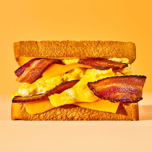 Delicious breakfast sandwich featuring bacon, eggs, and cheese between two slices of golden-brown toast against an orange background.