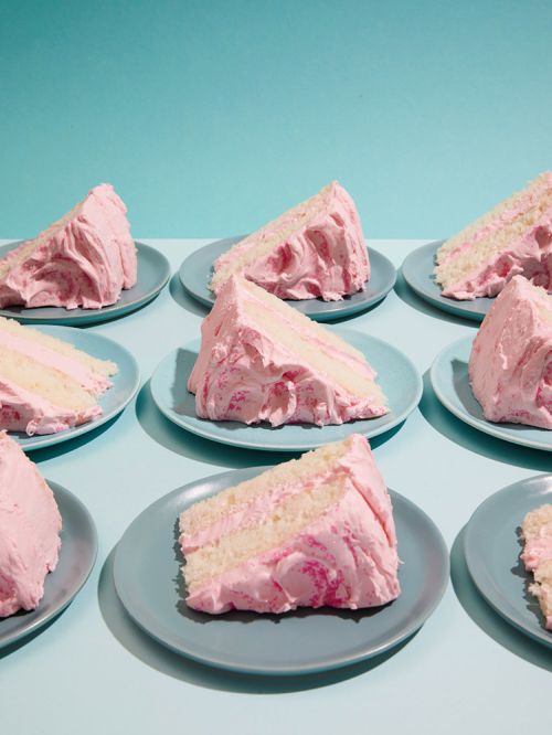 Rows of cake slices with pink frosting on blue plates, set against a teal background. Dessert photography with a symmetrical composition.
