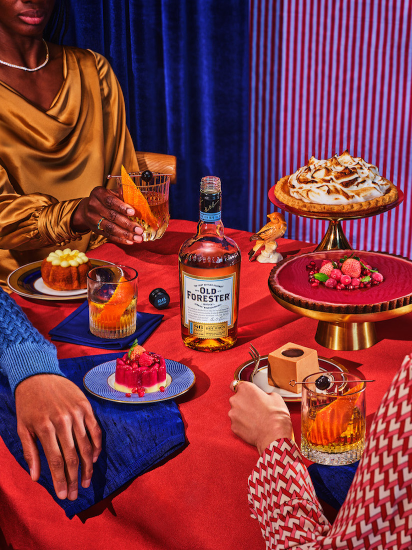 Still life of desserts and cocktails featuring an Old Forester bourbon bottle, displayed on a red tablecloth with colorful backgrounds.