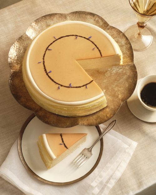 Overhead shot of sliced crepe cake on a decorative plate with coffee, sparkling wine, and flatware on a linen tablecloth.
