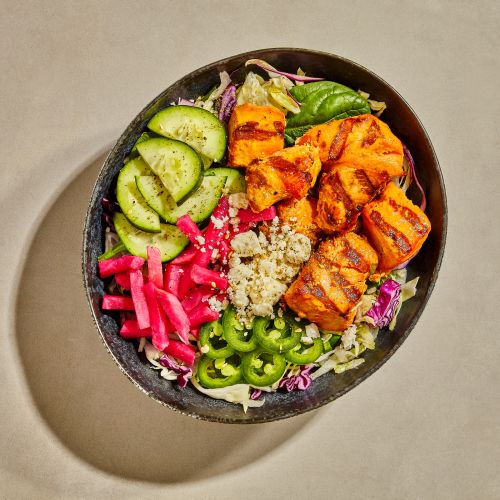 Overhead view of colorful salad bowl with grilled orange pieces, green cucumbers and jalapenos, and pink pickled onions.