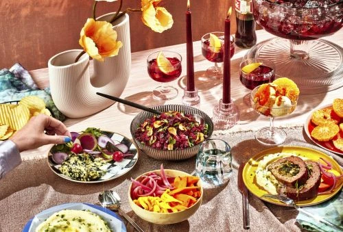 Overhead view of a table setting featuring assorted dishes, drinks, candles, and a vase of flowers in warm, inviting lighting.