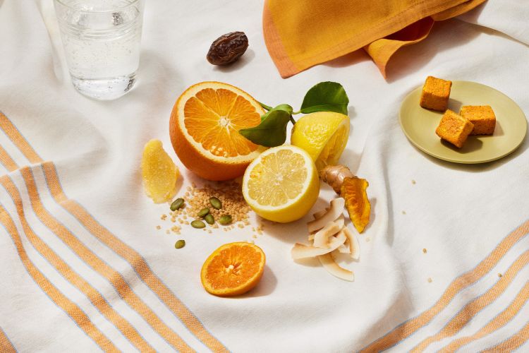Bright and cheerful food flat lay with oranges, lemons, dates, and candied ginger served on a white striped tea towel.
