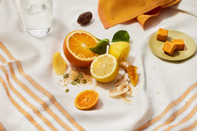Bright and cheerful food flat lay with oranges, lemons, dates, and candied ginger served on a white striped tea towel.