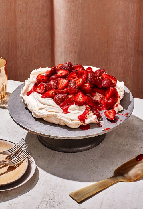 Overhead shot of a strawberry pavlova dessert on a grey stand, featuring meringue, cream, and fresh strawberries, with gold accents.