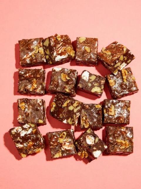 Overhead view of arranged rocky road squares on a pink background. Chocolate squares feature walnuts and marshmallows, arranged symmetrically.