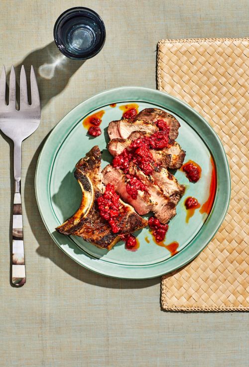 Overhead shot of a plate with sliced pork topped with red sauce, accompanied by a glass of water and woven placemat.