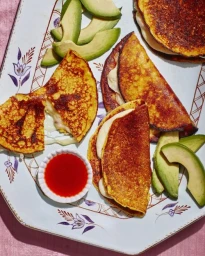 Top-down view of folded cheesy arepas on a patterned platter with sliced avocado and red sauce, styled by Sean Dooley