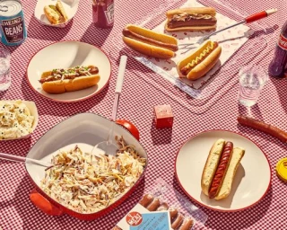 Top-down view of hot dogs, potato salad, coleslaw, and condiments on a red gingham tablecloth.