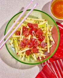 Bowl of diced tuna and apple salad with chopsticks, resting on a textured fabric surface with a small dish of sauce.