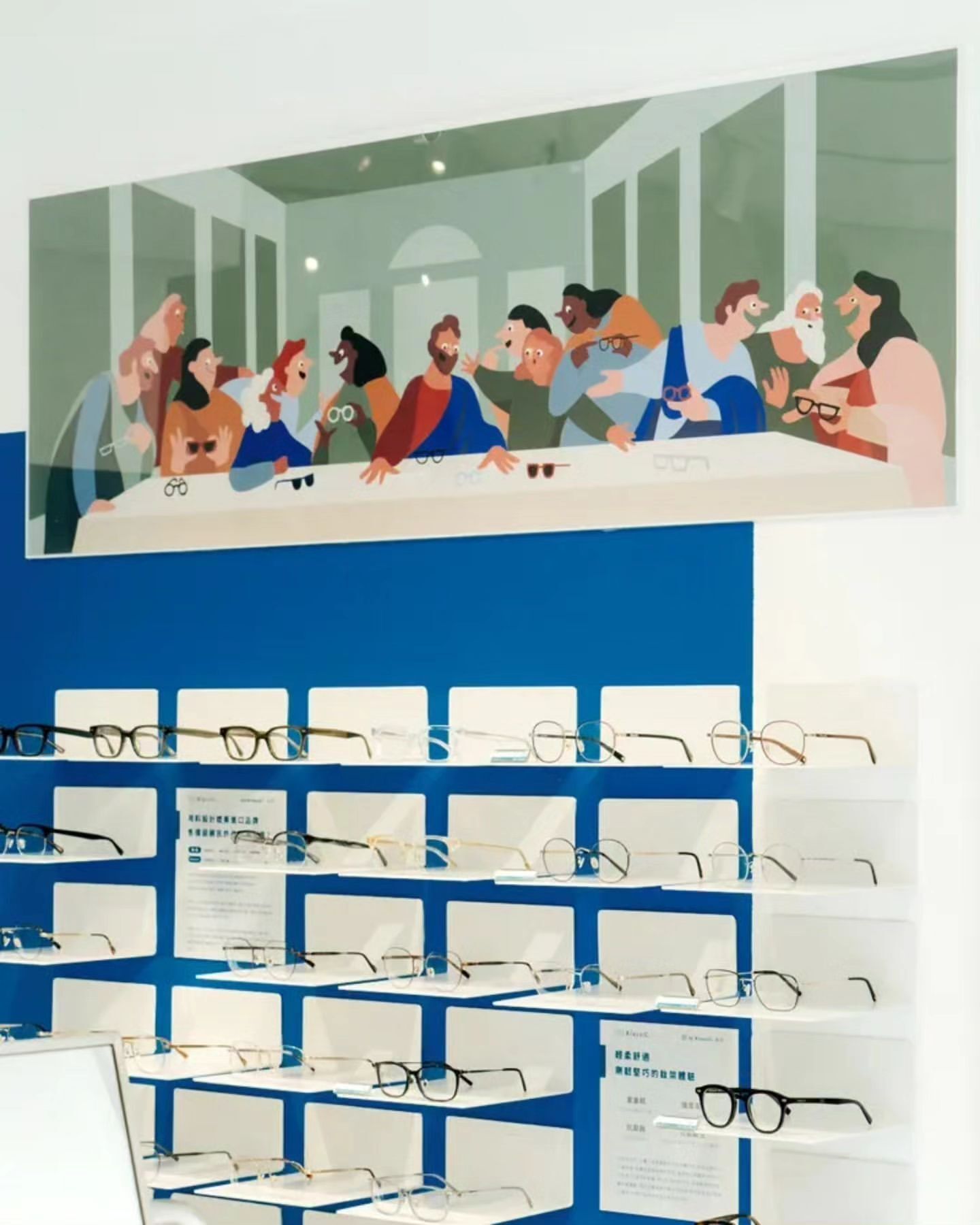 Eyeglass shop display with eyeglass frames on display shelves, and a painting of a dinner scene above the glasses.