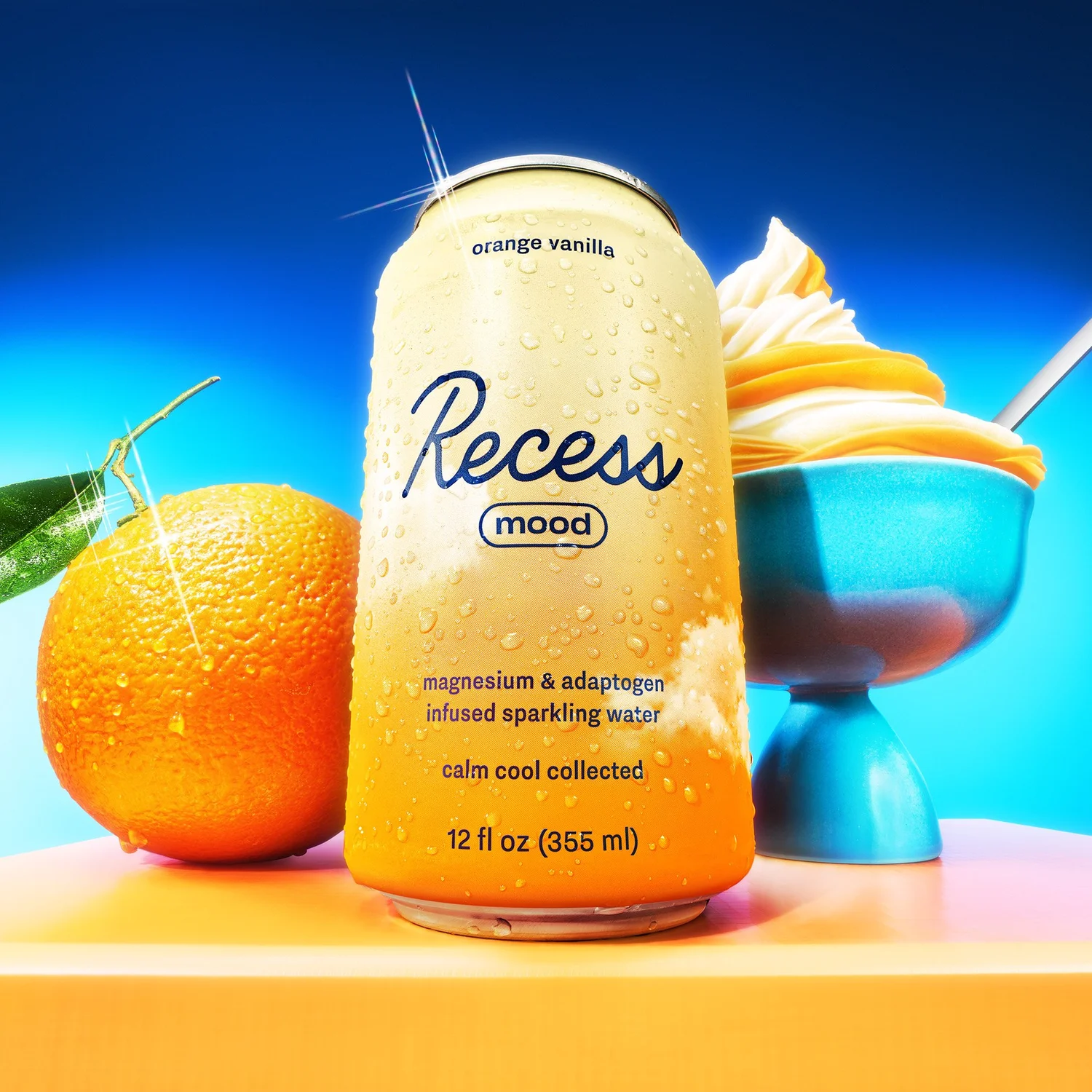 Recess mood drink can with orange vanilla flavor, water droplets, and a creamy dessert, vibrant blue background, and clean product shot.