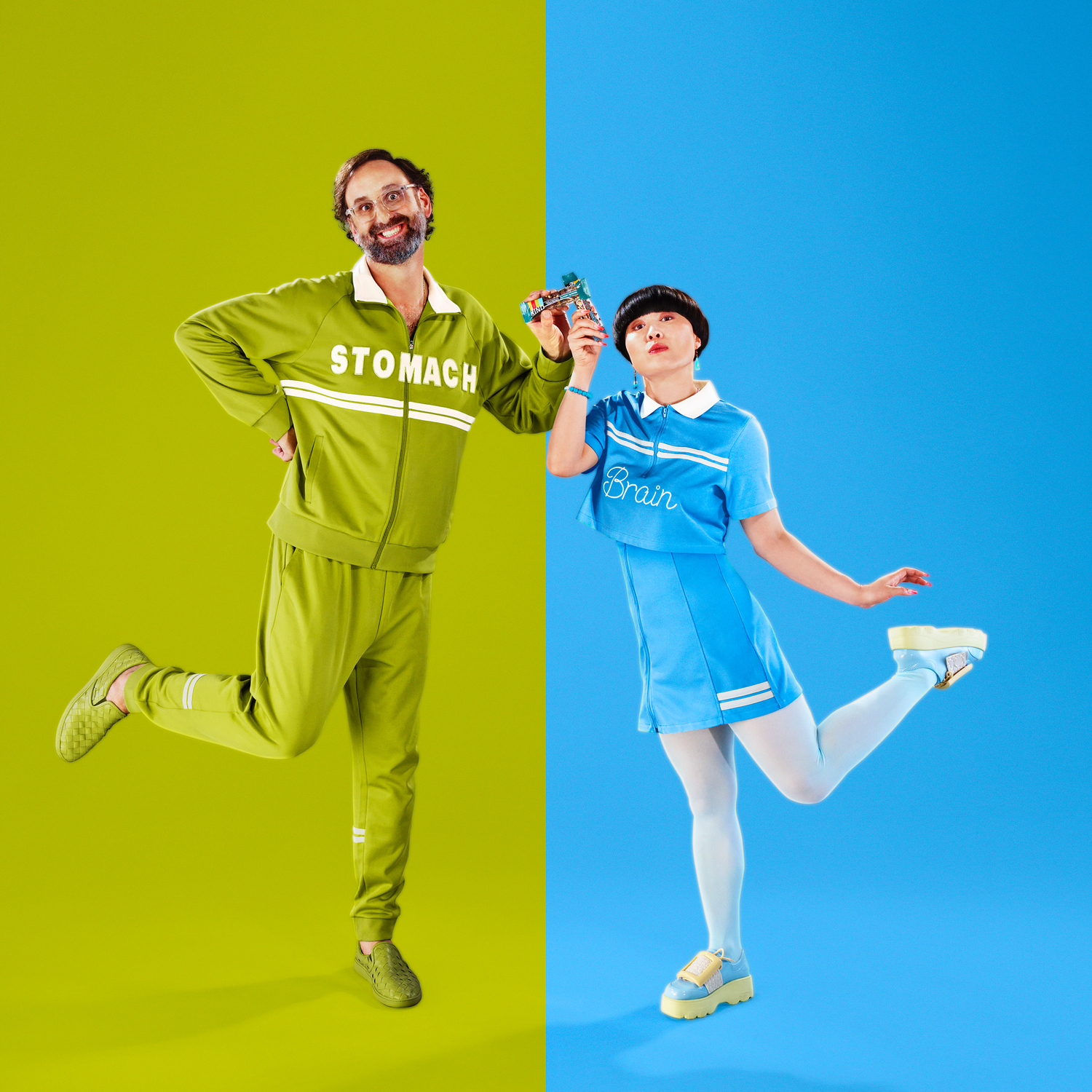 Two models strike a pose on a split green and blue background; one in a green tracksuit labeled 'STOMACH,' the other in a blue dress labeled 'Brain'