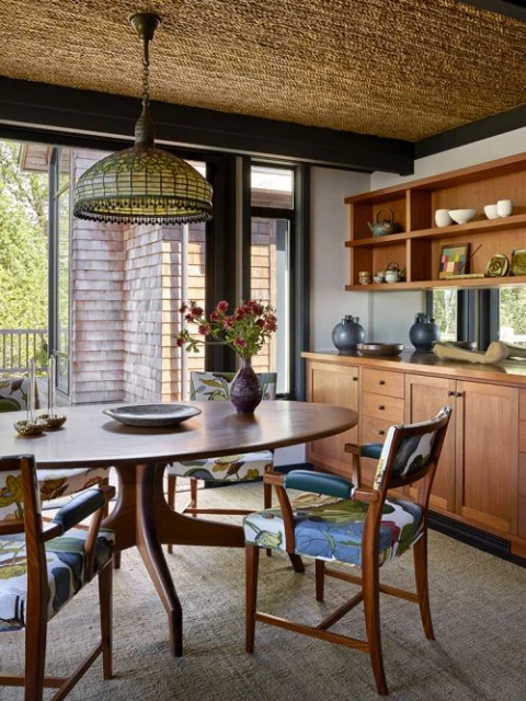 Dining room with oval wood table, floral upholstered chairs, chandelier, built-in wood cabinets, and jute rug in a warm interior setting.