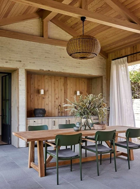 Indoor dining area with wooden table, green chairs, and woven pendant light under a wooden ceiling, creating a warm, inviting ambiance.