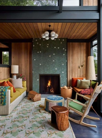 Living room interior featuring a yellow couch, patterned rug, fireplace, and rocking chair, with wood paneled walls and natural light.