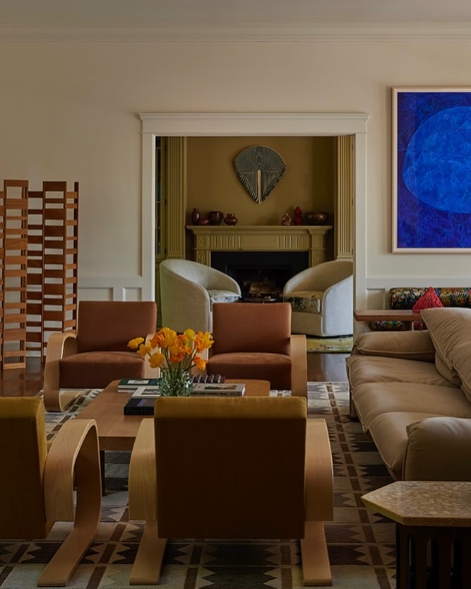 Living room interior showcasing four armchairs, a beige sofa, a coffee table with flowers and books, and an abstract painting.