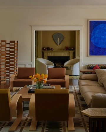 Living room interior showcasing four armchairs, a beige sofa, a coffee table with flowers and books, and an abstract painting.