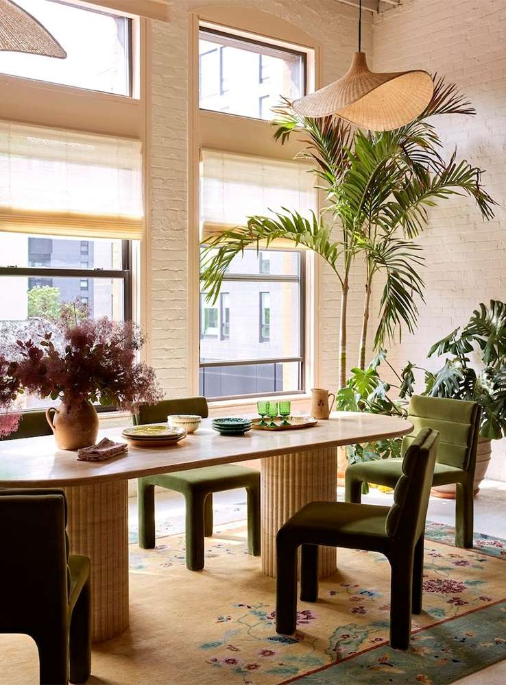 Indoor dining area with a large dining table, green chairs, and indoor plants near windows creating a bright and inviting atmosphere.