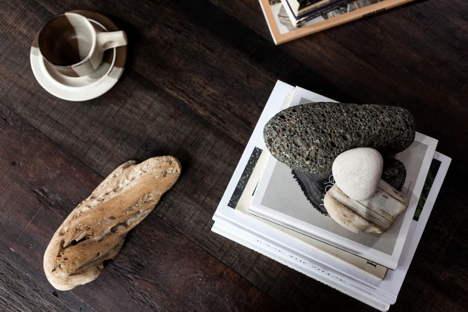 Overhead interior still life featuring books, smooth stones, and a ceramic coffee cup on a dark wooden table.