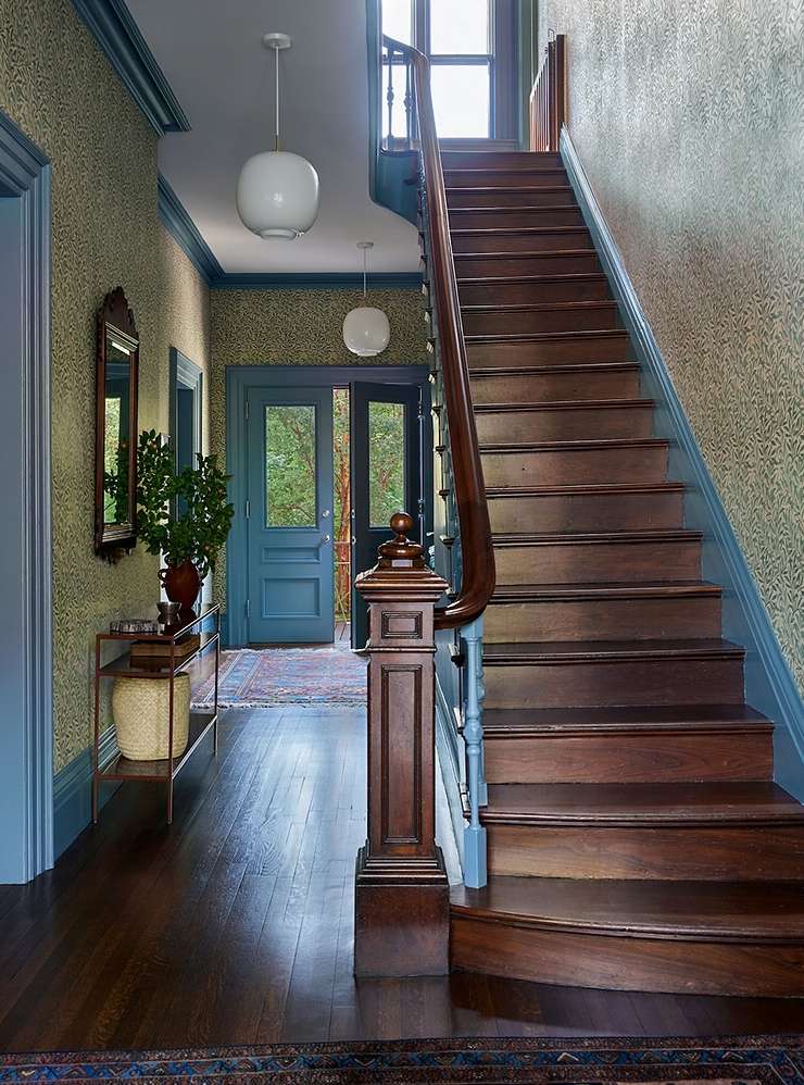 Interior view of a home's foyer with a wooden staircase, blue trim, patterned wallpaper, pendant lights, and an open doorway.