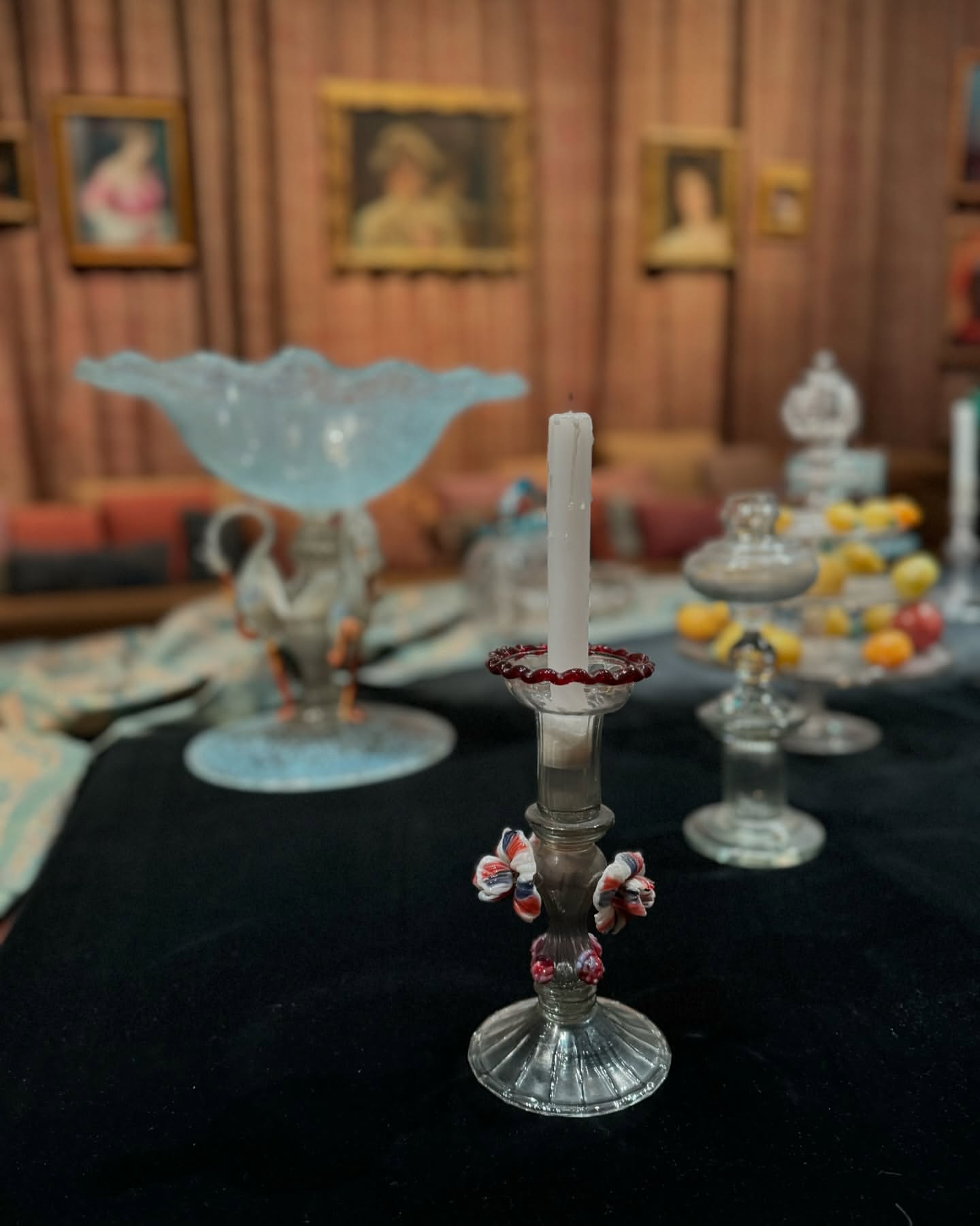 Elegant table centerpiece with antique glass candle holder, tall white candle, and decorative floral accents in a vintage setting.
