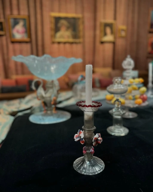 Elegant table centerpiece with antique glass candle holder, tall white candle, and decorative floral accents in a vintage setting.