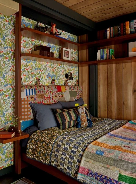 Bedroom corner with a wood-paneled wall, open shelves, and a bed featuring patterned quilts and cushions, creating a cozy ambiance.