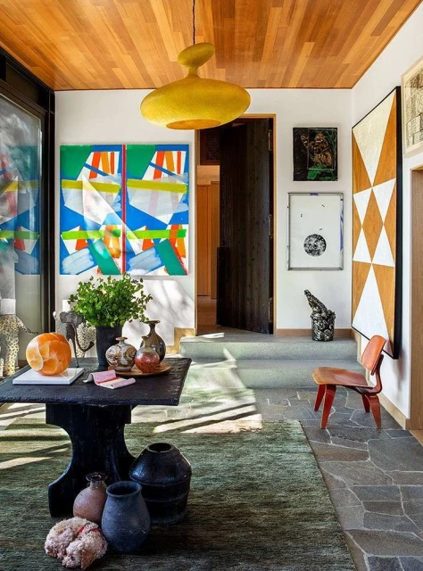 Interior view showcases an eclectic mix of furniture, bold abstract artwork, and unique decorative objects in a sunlit entryway.