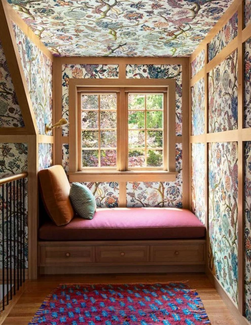 Indoor reading nook with a window seat, floral wallpaper on the walls and ceiling, hardwood floors, and natural light coming in from the window.