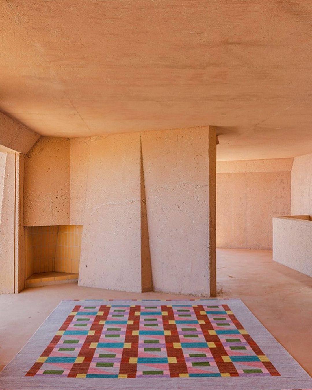 Interior design with colorful rug in a peach-toned room featuring textured walls, indirect natural light, and concrete architectural details.