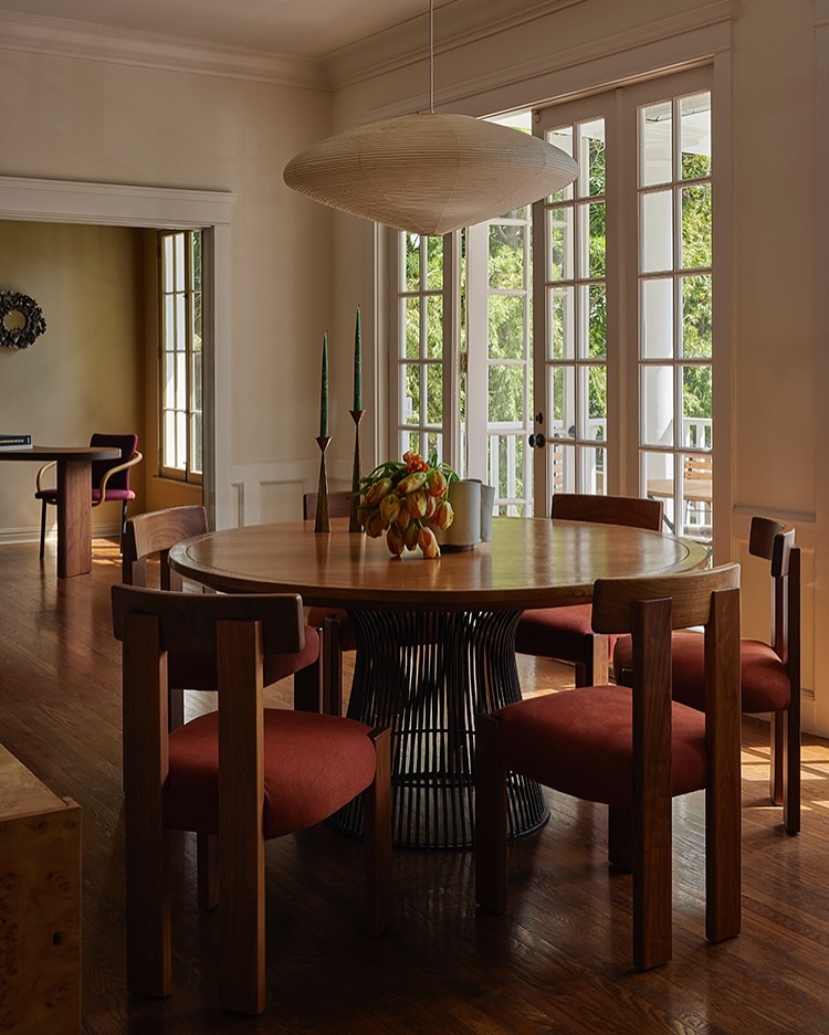 Dining room features a round wooden table, red upholstered chairs, overhead light fixture, and sunlight streaming through the windows.