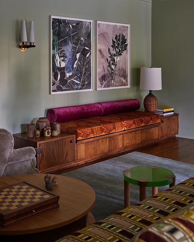 Living room interior showcases a wooden daybed with vibrant cushions, complemented by framed botanical art and soft lighting. 