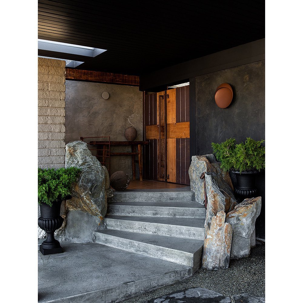 Exterior view of concrete steps leading to a wooden door, flanked by rock formations and potted plants in a modern home design.