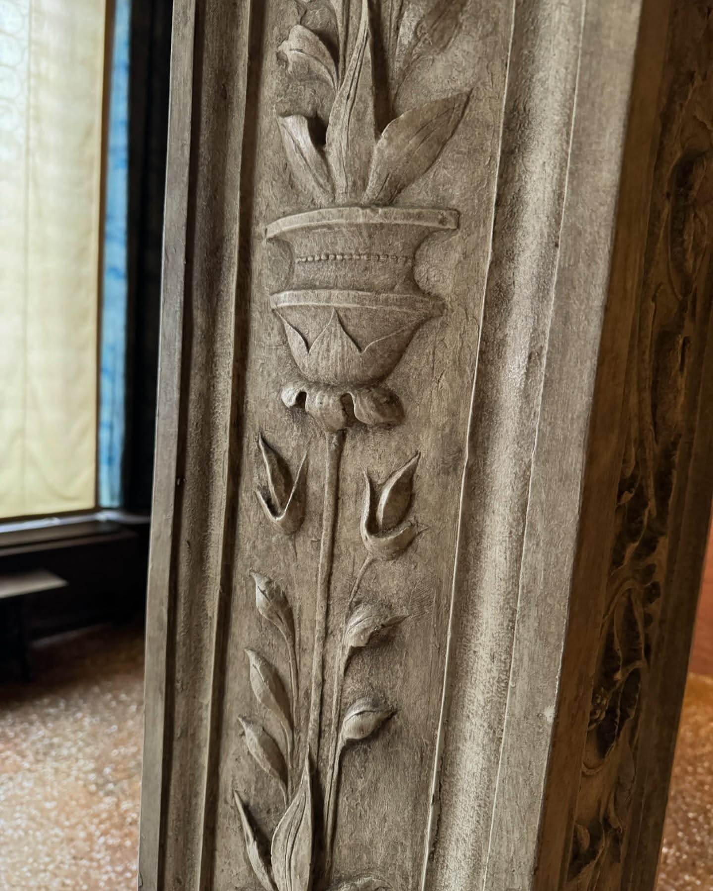 Close-up of carved stone column with floral design and decorative vase motif, stone textured, neutral color palette, indoor setting, ornate detail.