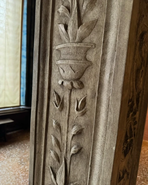 Close-up of carved stone column with floral design and decorative vase motif, stone textured, neutral color palette, indoor setting, ornate detail.