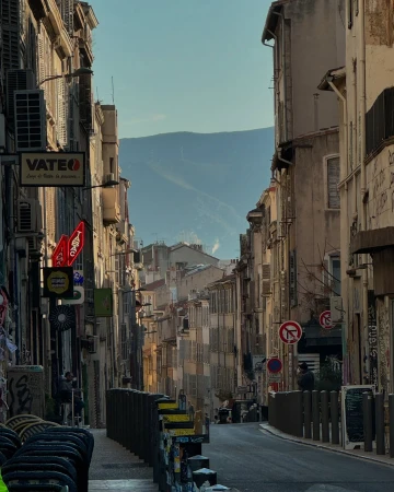 Urban streetscape in Europe featuring old buildings, signs, and mountain backdrop on a sunny day. Architecture and city life converge.