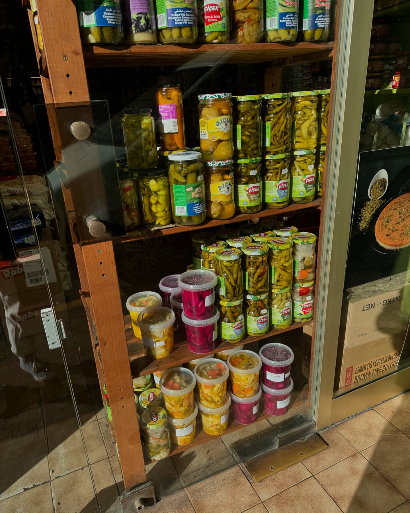 Shelves filled with jars and plastic containers of pickled vegetables, including cucumbers and peppers, on display for sale.