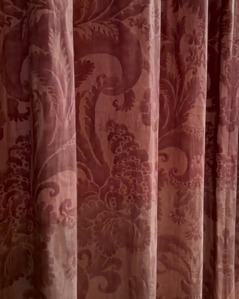 Intricate floral pattern on deep red fabric curtains, showcasing texture and classic design in a dimly lit, indoor setting.