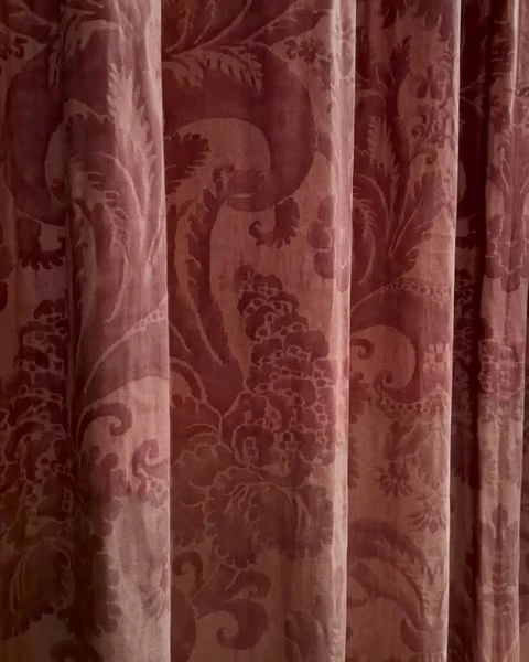 Intricate floral pattern on deep red fabric curtains, showcasing texture and classic design in a dimly lit, indoor setting.