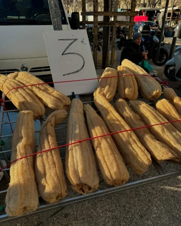Display of loofah sponges for sale outdoors on a wire rack under a sign with a price of 3 Euros in a market, daytime.