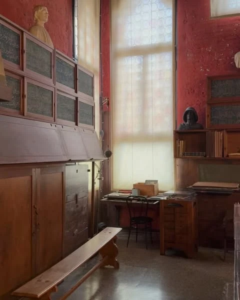 Indoor scene features a wooden bench, desk with chair, cabinets, and busts, highlighted by a large window that provides natural lighting.