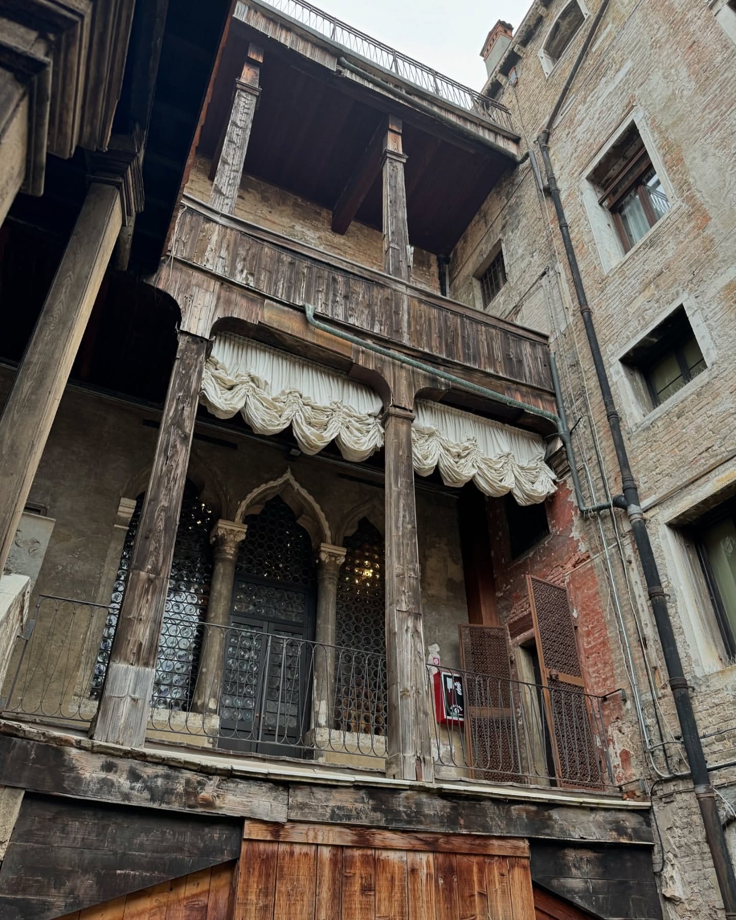 Exterior view of a weathered building with a wooden balcony and ornate windows, showcasing architectural details and old-world charm.