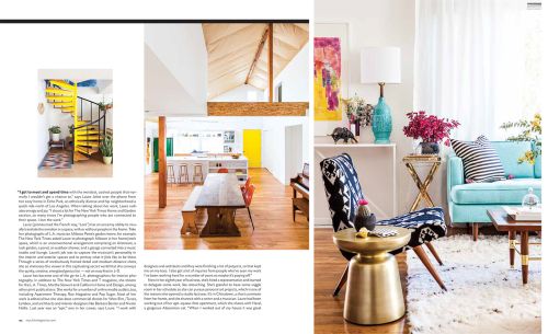 Interior shot of living room and kitchen featuring blue couch, patterned chair, gold side table, dining table, and yellow spiral staircase.