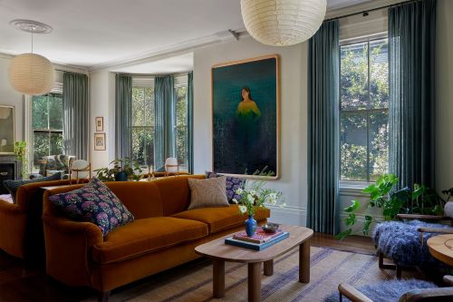 Stylish living room showcases an orange sofa with patterned cushions, alongside a wooden coffee table and vibrant artwork.