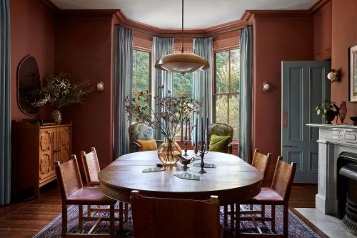 Warm-toned dining room interior featuring a wooden table set with decor, surrounded by leather chairs, with natural light from windows.