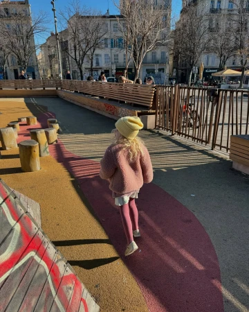 Child in pink fleece jacket and yellow beanie walking away in a public square by photographer Laure Joliet