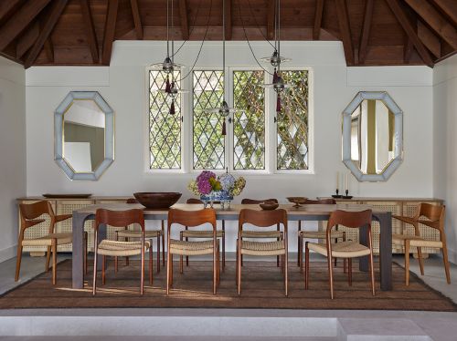 Dining room featuring a wooden table with brown chairs, illuminated by pendant lights, with a large area rug and neutral wall paint.