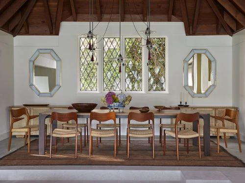 Dining room featuring a wooden table with brown chairs, illuminated by pendant lights, with a large area rug and neutral wall paint.